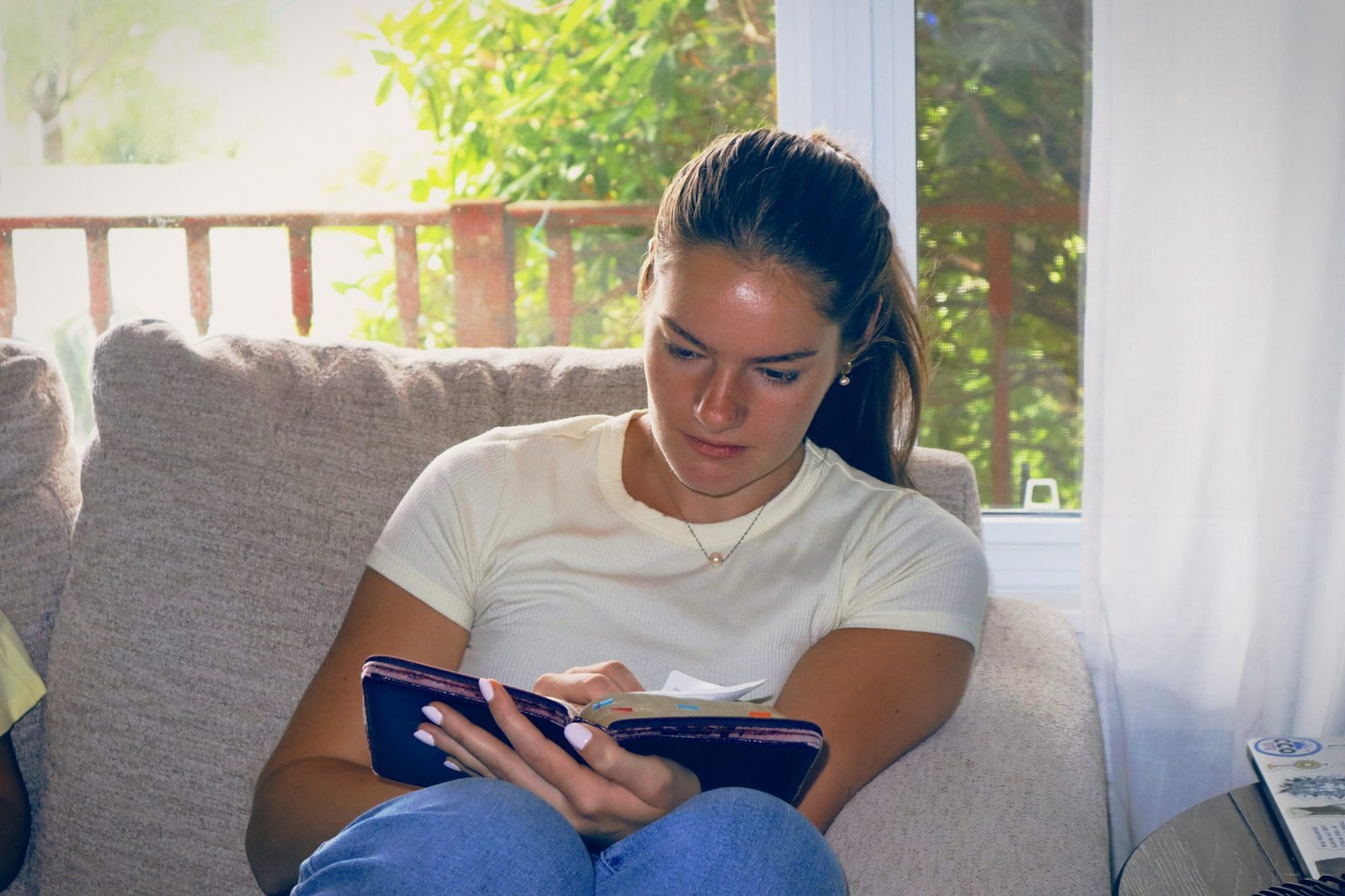 A woman writing in a journal on a sunlit couch.
